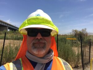 Engineer standing in field wearing hard hat and sunglasses,